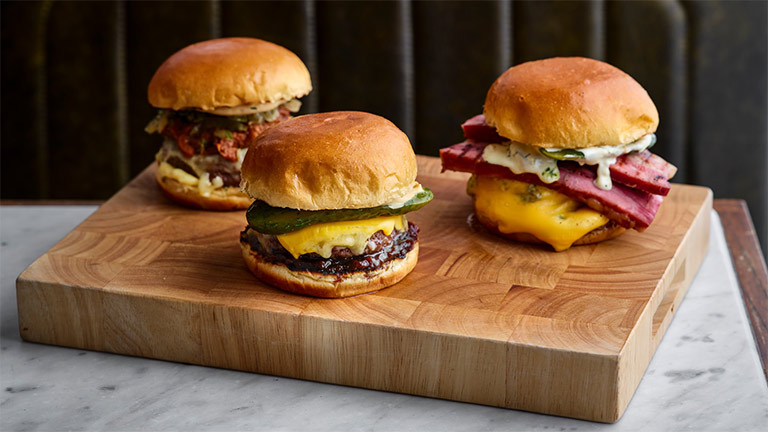 Three burgers on a wooden block at The Butcher's Tap and Grill