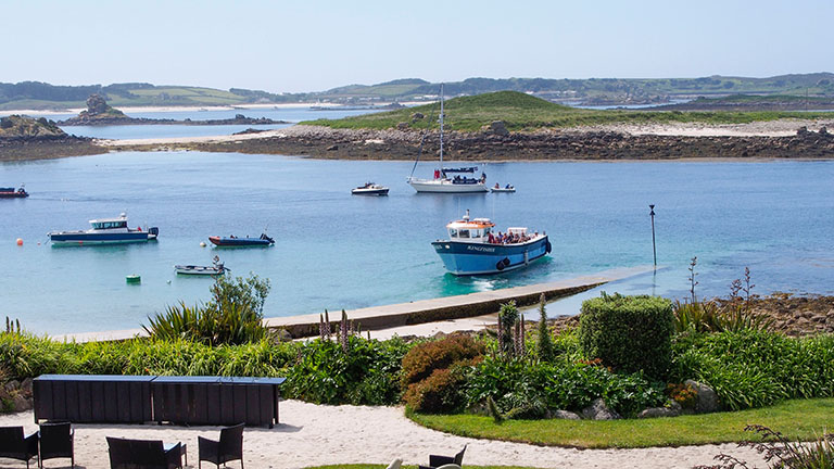 A view of the Isles of Scilly on a sunny day with boats in the midground and islands in the background