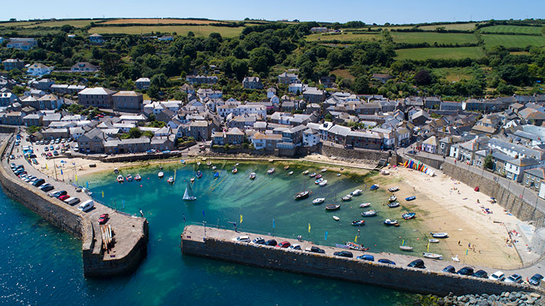 A picturesque aerial view of Mousehole village overlooking the townhouses, sandy beach, harbour and turquoise sea