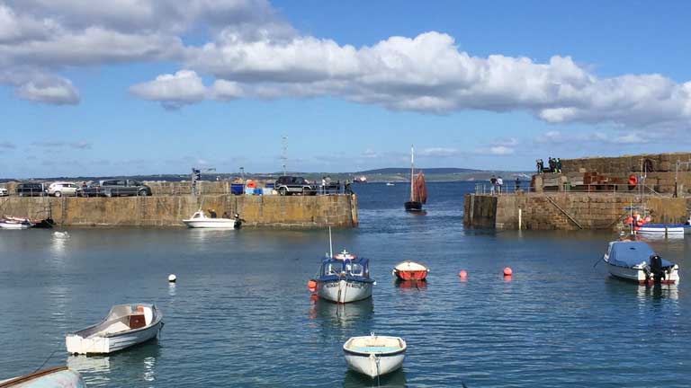Boats on calm water in Mousehole harbour under blue skies