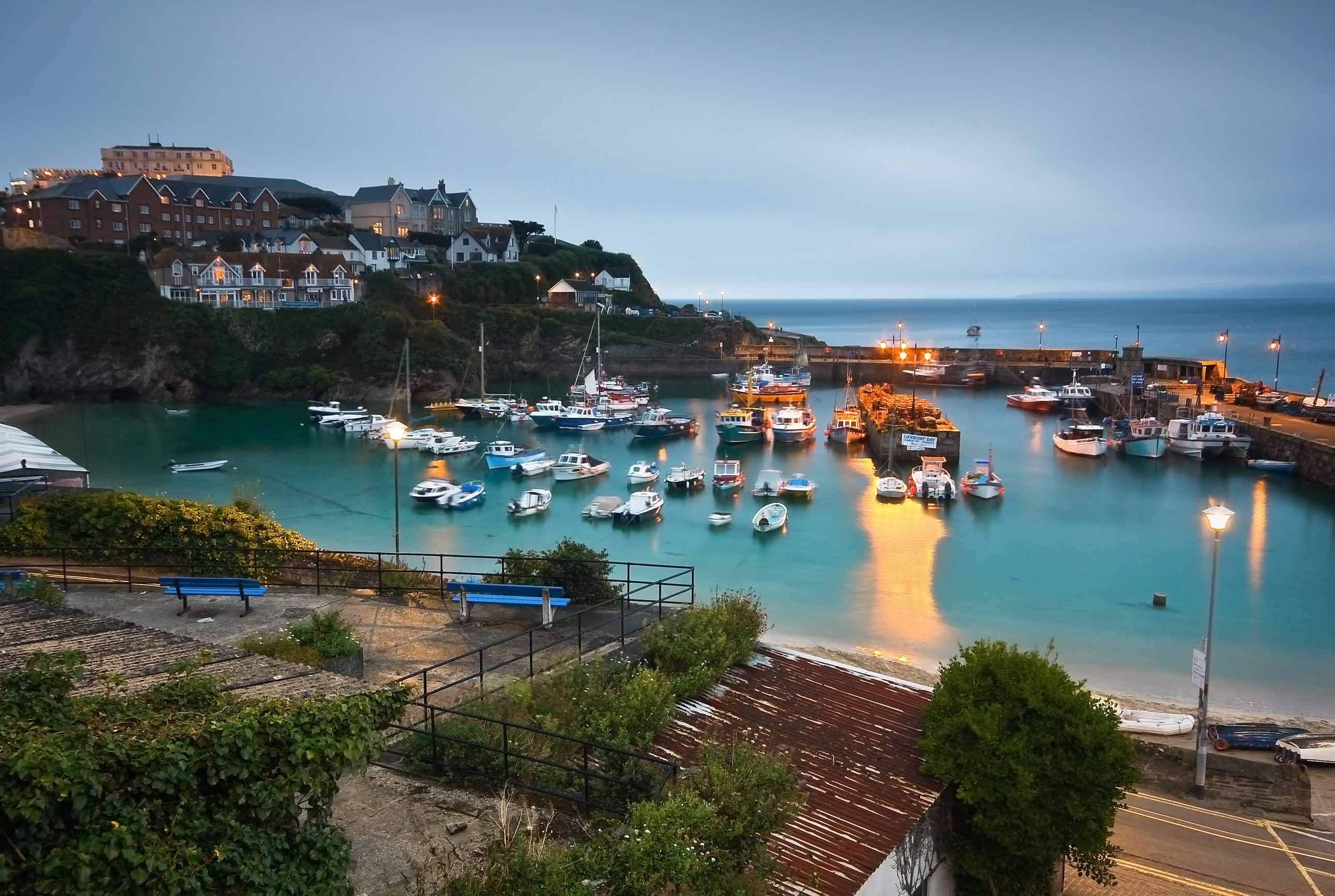 Newquay harbour at dusk with lights illuminating the boat-peppered water