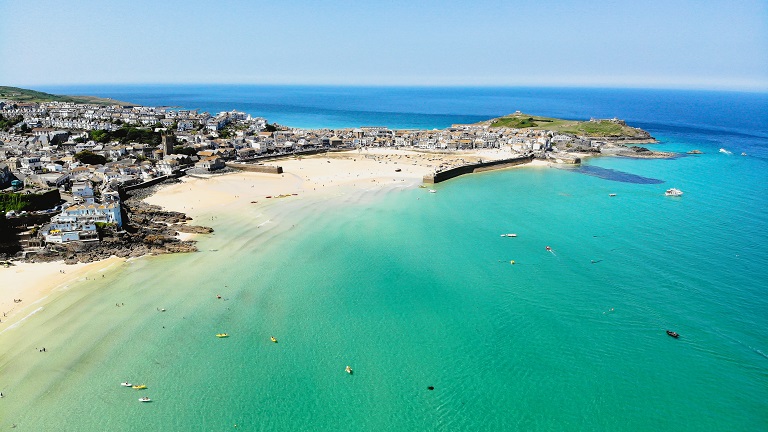 A beautiful view over St Ives showing the town's beaches, white sands, turquoise seas and harbour at low tide.