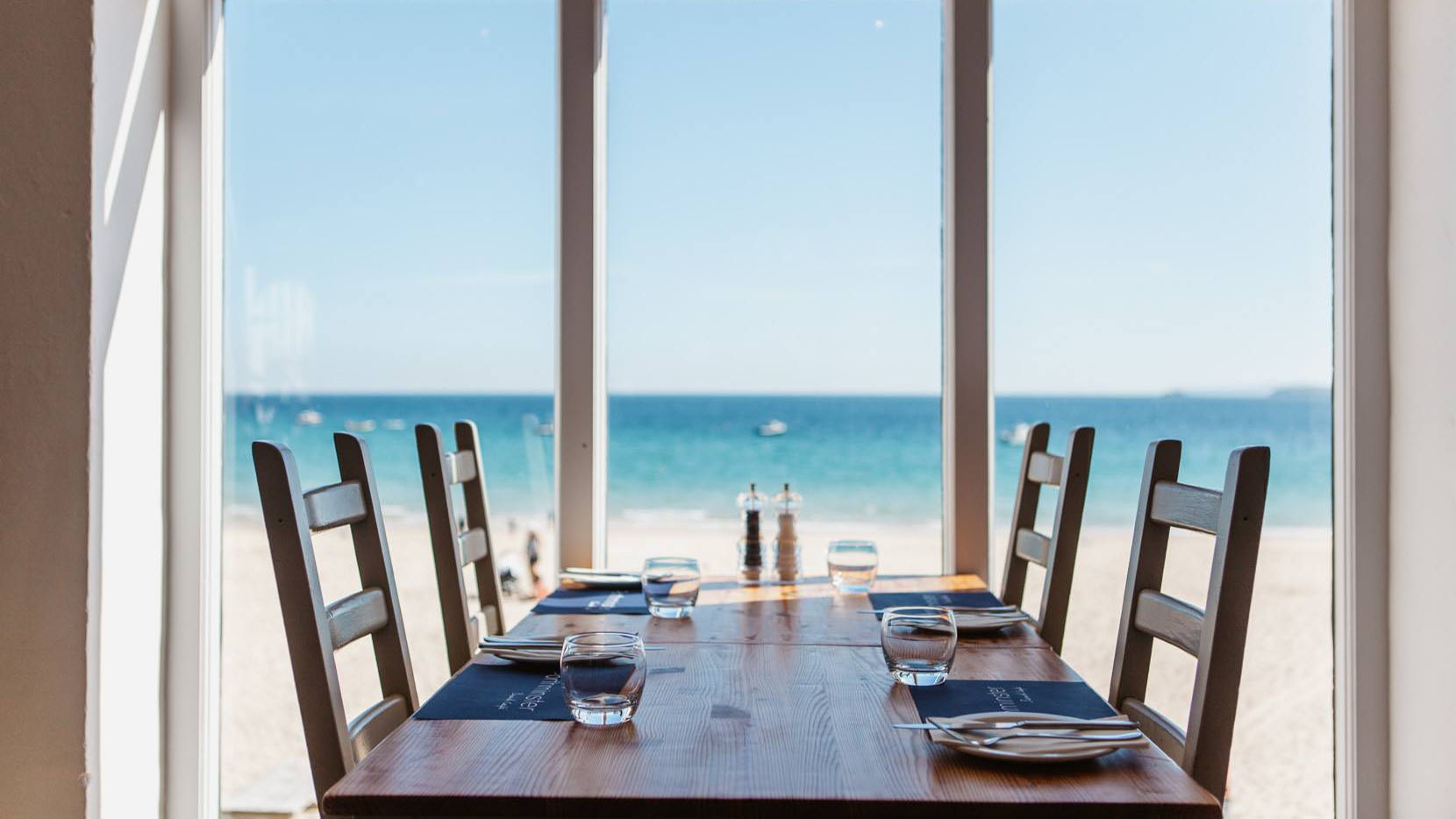 A table and chairs by the window at Porthminster Beach Cafe with gorgeous sea and beach views in St Ives