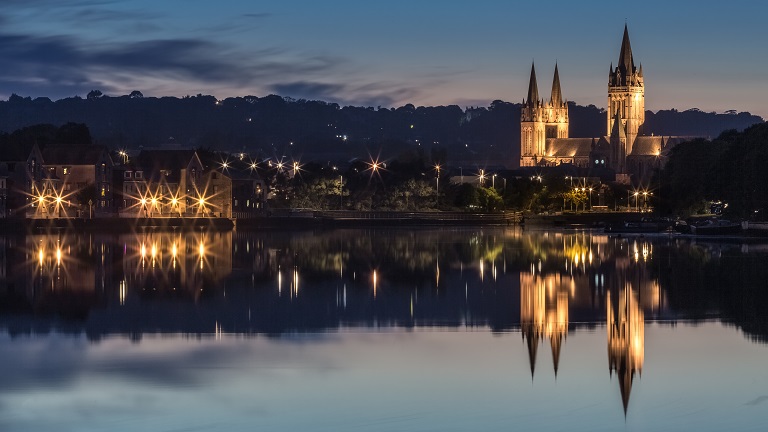 A view of Truro at dusk with the lights of the city and the cathedral reflected in the calm water of the river