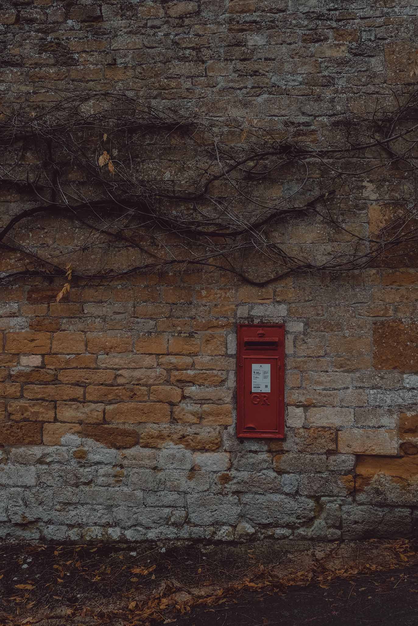 A bright red post box set within a honey coloured wall in the Cotswolds