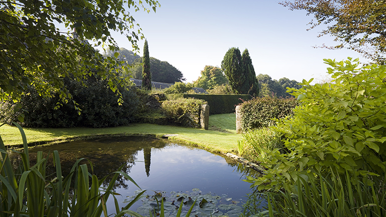 A view of the grounds of Buckland Abbey with a pretty pond, mown lawns, shrubs and trees