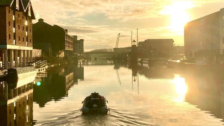 A motor boat heading off down the historic Gloucester quay at sunrise