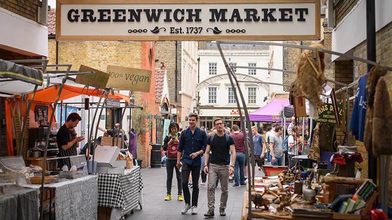 The busy Greenwich Market full of people and stalls with an antique sign hanging overhead