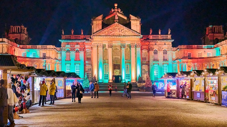The front of Blenheim Palace illuminated by lights at night-time during one of their Christmas markets