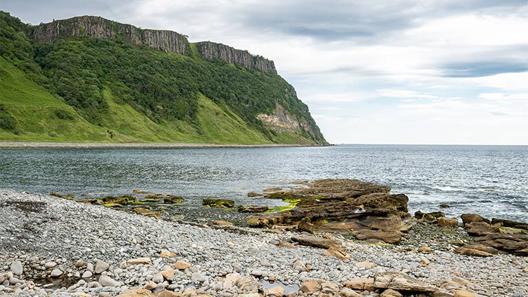 The shingle beach with towering green cliffs in the background of Bearreraig Bay on the Isle of Skye