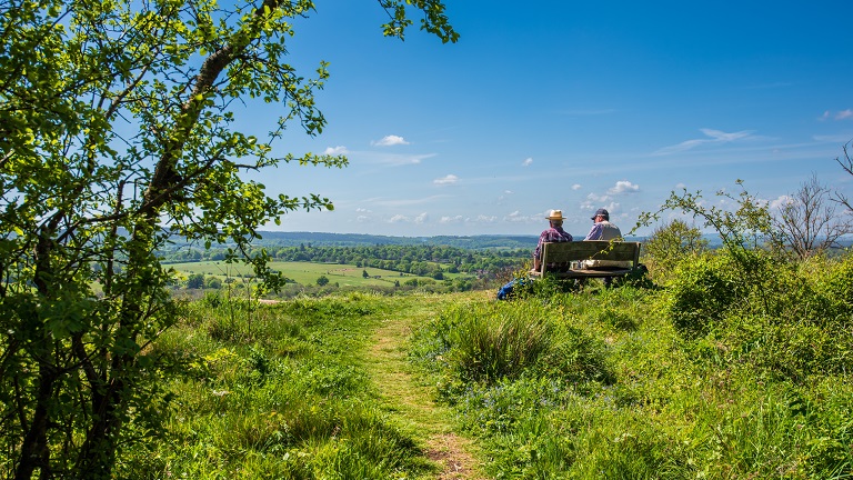 Two friends sitting on a bench overlooking the views on the North Downs Way