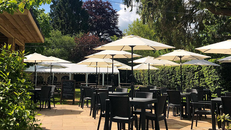 The suntrap garden patio of the Abinger Hatch gastropub in Dorking, with tables, chairs and parasols in the sunshine