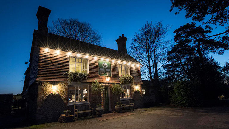 The spot-lit Three Horseshoes pub in Thursley in the evening 