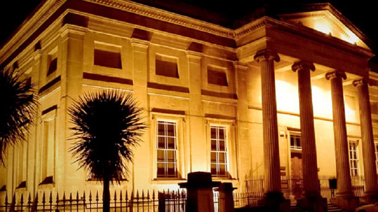 The facade of Swansea Museum at night-time, illuminated by warm spotlights 