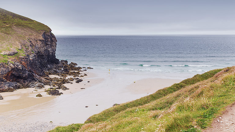 The sandy beach of Chapel Porth sandwiched between grass-covered cliffs between St Agnes and Porthtowan