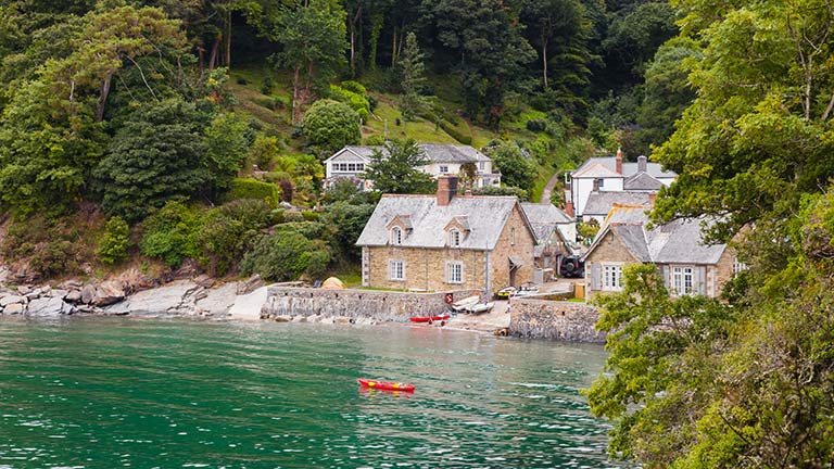 Durgan beach covered at high tide and overlooked by a clutch of pretty cottages