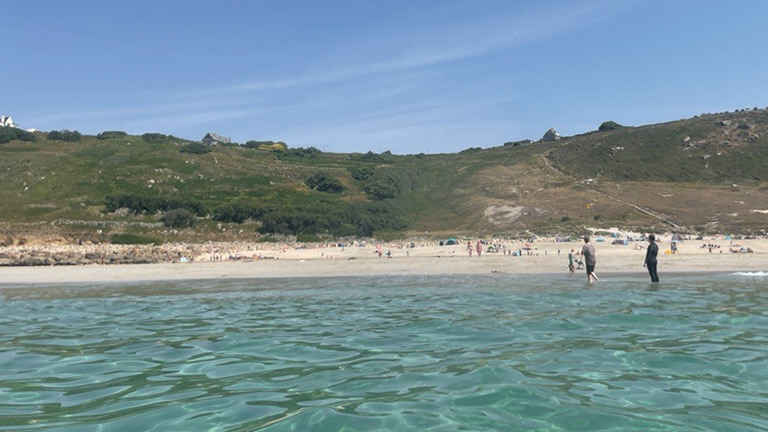 A grass-backed beach with golden sand and clear water at Gwynver in Cornwall