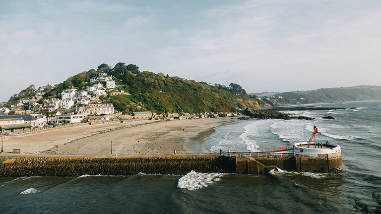 Looe Beach in Cornwall with the town's pier in the foreground and houses in the background