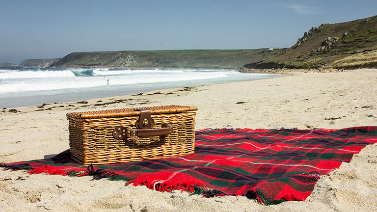 A picnic hamper on Sennen Beach with the sea and cliffs in the background