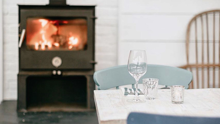 A dining table with sparkling glasses next to a crackling wood burning stove at Amelie, Porthleven