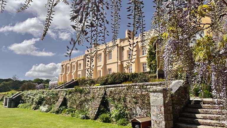 The sun-kissed façade of Pentillie Castle framed by flowering trees under bright blue skies