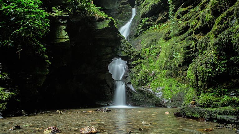 A small waterfall flowing into a glassy kieve at St Nectan's Glen near Tintagel