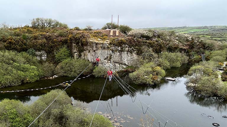 Two people zip lining across the historic quarry at Via Ferrata in Cornwall