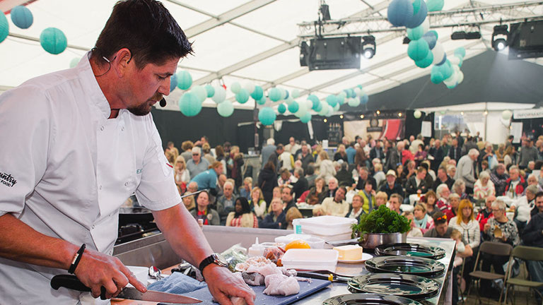 A chef preparing seafood in front of a seated audience at Falmouth Oyster Festival