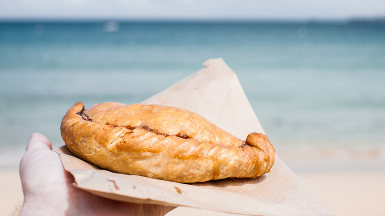 A Cornish pasty with a coastal background of turquoise seas