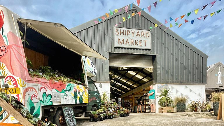 The exteriors of The Shipyard Market with colourful fruit stalls and bunting