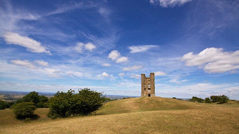 A view of Broadway Tower on a balmy day with blue skies and tufty white clouds