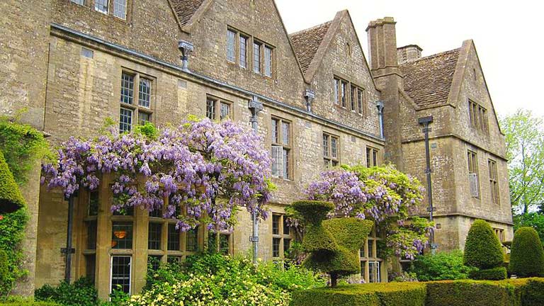 The golden-stoned exterior of Rodmarton Manor with flowers and topiaries out front