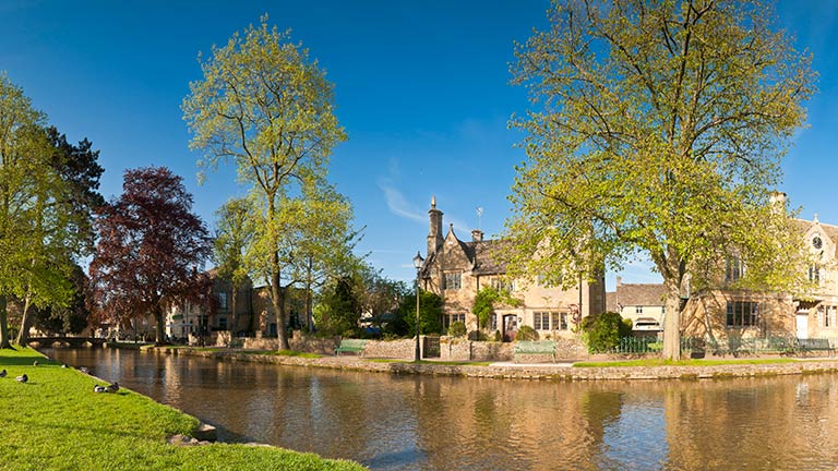 The yellow stone cottages and winding river of Bourton-on-the-Water in the Cotswolds under blue skies