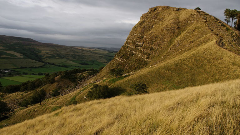 A view of rolling hills and a steep cliff in the Peak District
