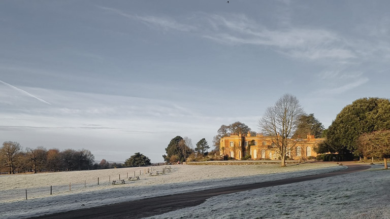 A view of Killerton House with frost-tinged grounds under blue skies