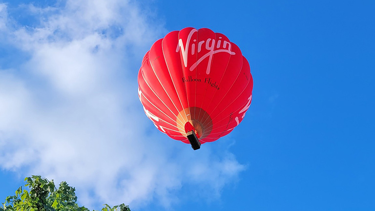 One of Virgin's iconic red balloons taking flight under blue skies in Devon
