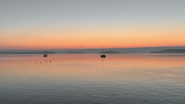 A sunset view over Studland Bay with boats silhouetted on the horizon