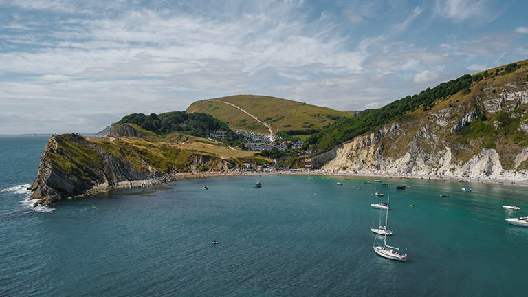 A view of the stunning Lulworth Cove with boats bobbing in its natural harbour