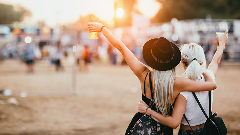 Two festivalgoers with drinks in hand arriving at a festival