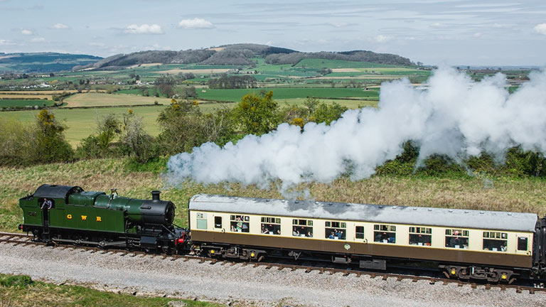 A Gloucestershire Warwickshire Steam Railway train chugging through verdant countryside