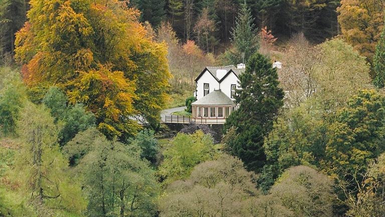 An exterior view of The Cottage in the Wood in Braithwaite surrounded by autumnal trees