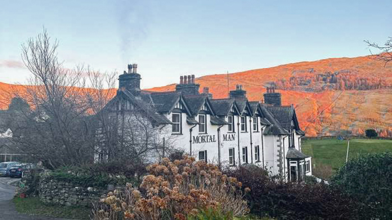 The exteriors of the Mortal Man in Troutbeck with bracken-covered fells in golden hour sunlight behind