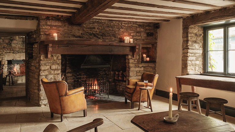 Two armchairs arranged next to the glowing fireplace in The Bull, Charlbury
