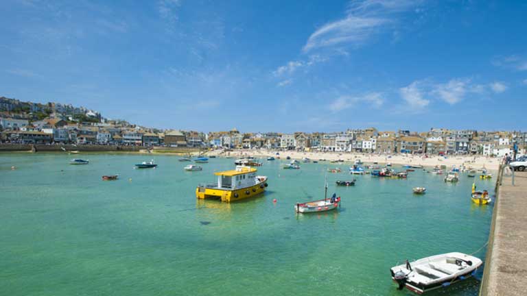 Overlooking the town of St Ives in West Cornwall. Boats bob on the crystal-clear waters of St Ives harbour and fishermen's cottages, shops and cafes line the background. 
