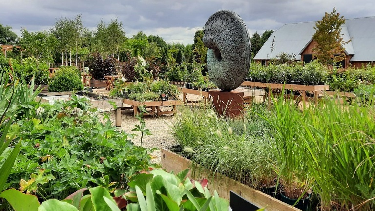 The garden of the Yurt at Nicholsons in Oxfordshire with flower beds, home-grown plants and a striking sculpture