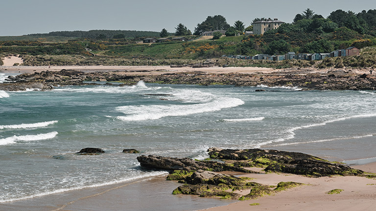 The sandy shores of Hopeman East Beach overlooked by beach huts