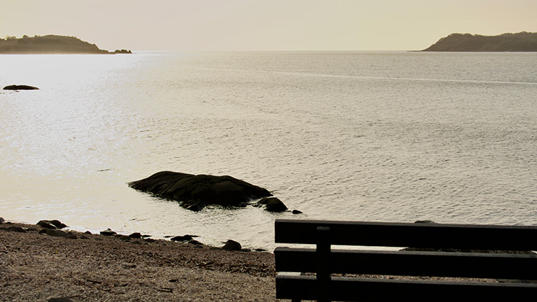 A bench overlooking Kippford Beach at sunset