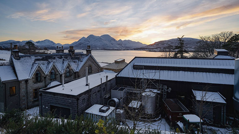 A view of Raasay distillery reached from the Isle of Skye, with a beautiful loch and snowy mountains in the background