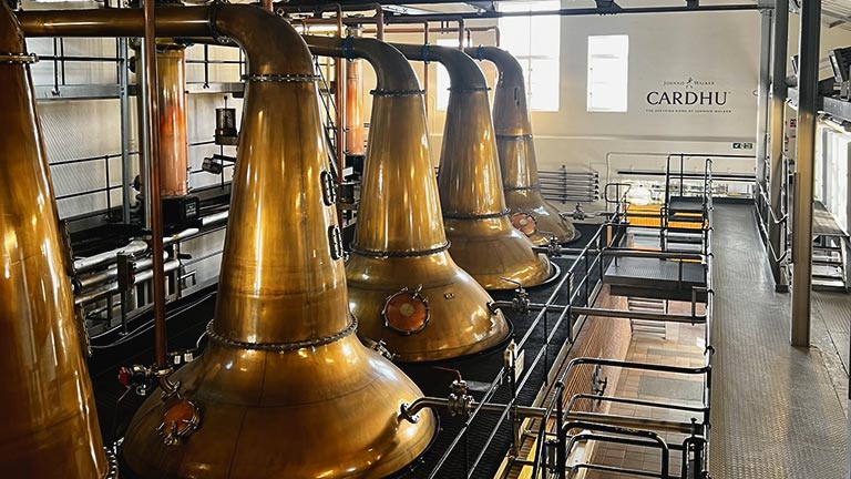 Copper-hued distilling vats in a row inside Cardhu Distillery