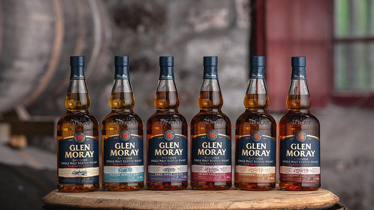 A row of Glen Moray whisky bottles atop an oak barrel